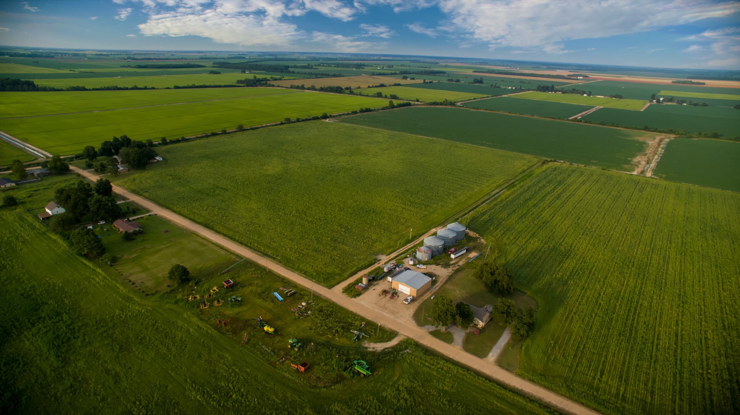Aerial view of Arkansas Delta farmland with grain bins, a farmhouse, and fields running to the horizon