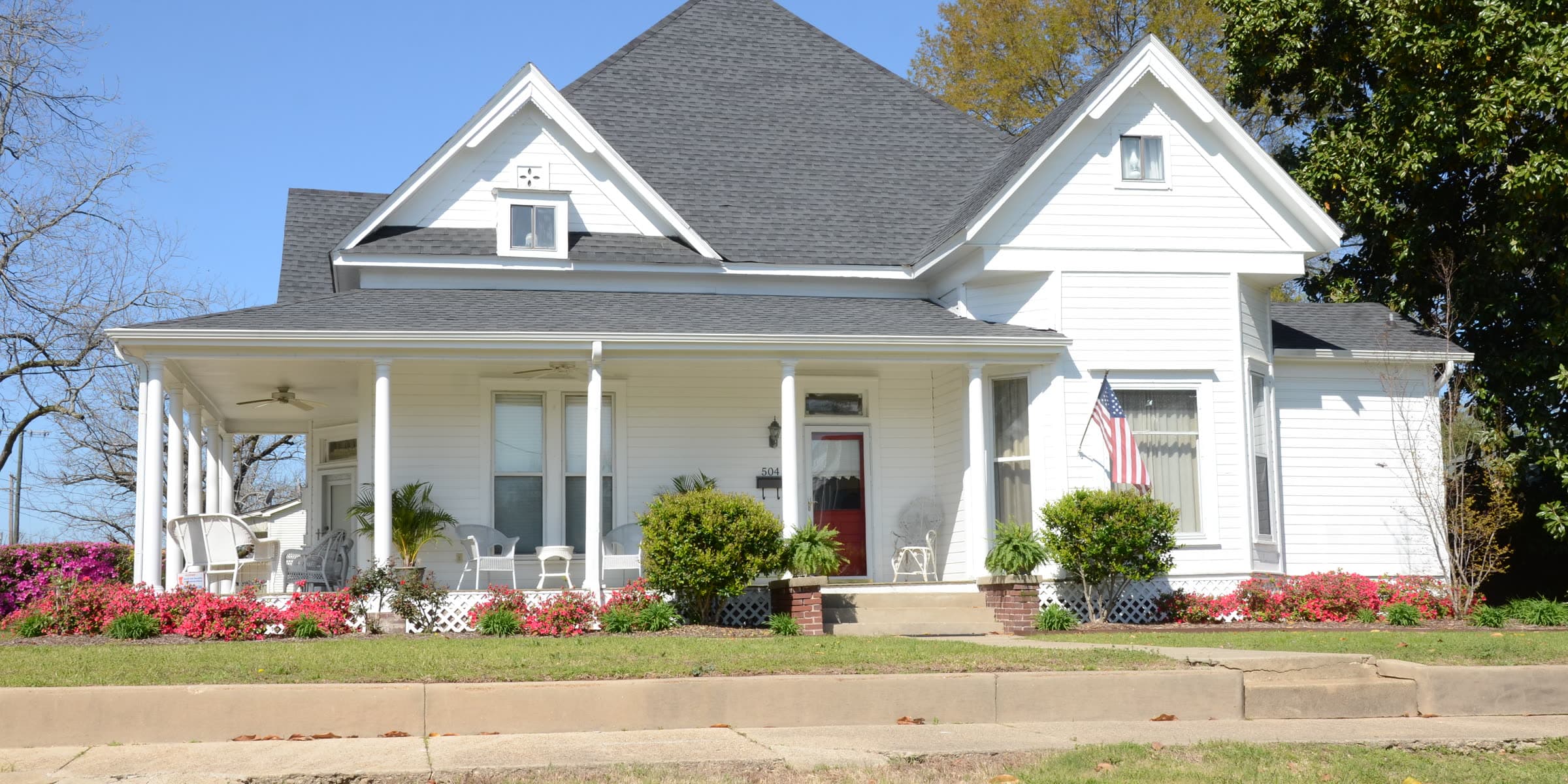 A white Victorian home with a wraparound porch and blooming azaleas in El Dorado, Arkansas